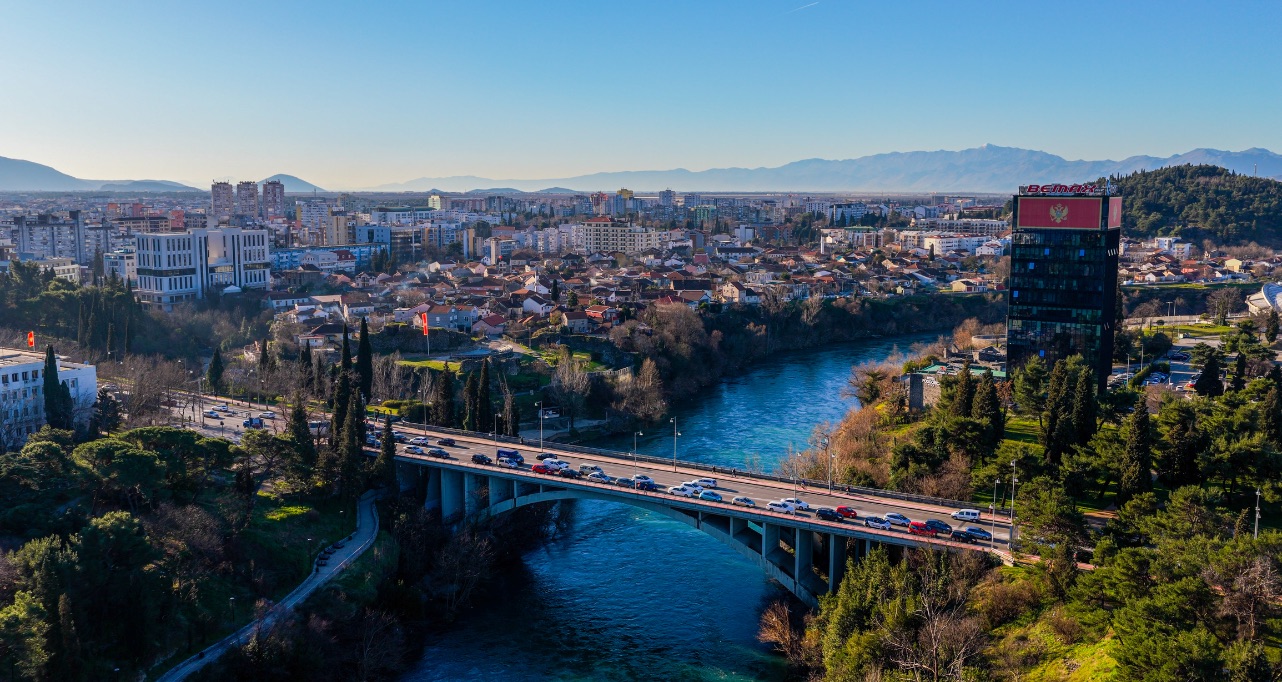 Aerial view of Podgorica city with bridge over Moraca River and dense urban skyline, modern capital city surrounded by green landscape and mountains in Montenegro